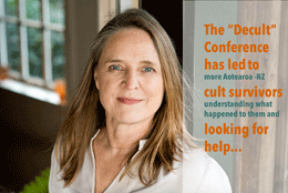 A middle aged long blond haired woman stands in a light room with indoor plants