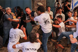A crowd of young men wearing Israeli flag day t-shirts aim kicks at a journalist