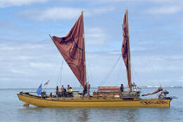A twin-hulled two-sailed waka rests in still waters